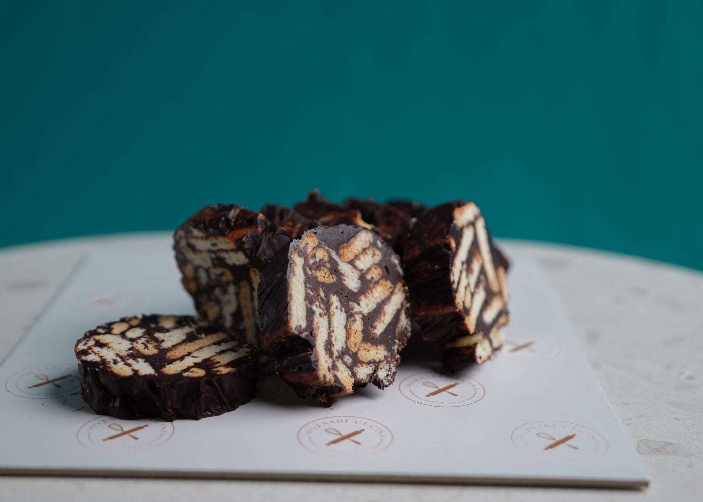 Chocolate and white layered cookies on a white surface with a teal background