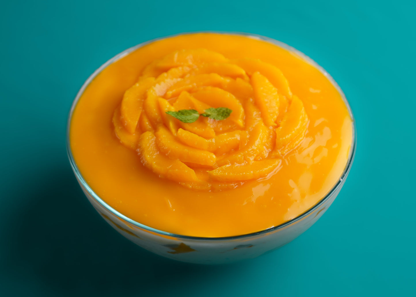 A top view of a Mango Trifle dessert with layers of cake and cream, garnished with a mango rose on top, on a teal background.