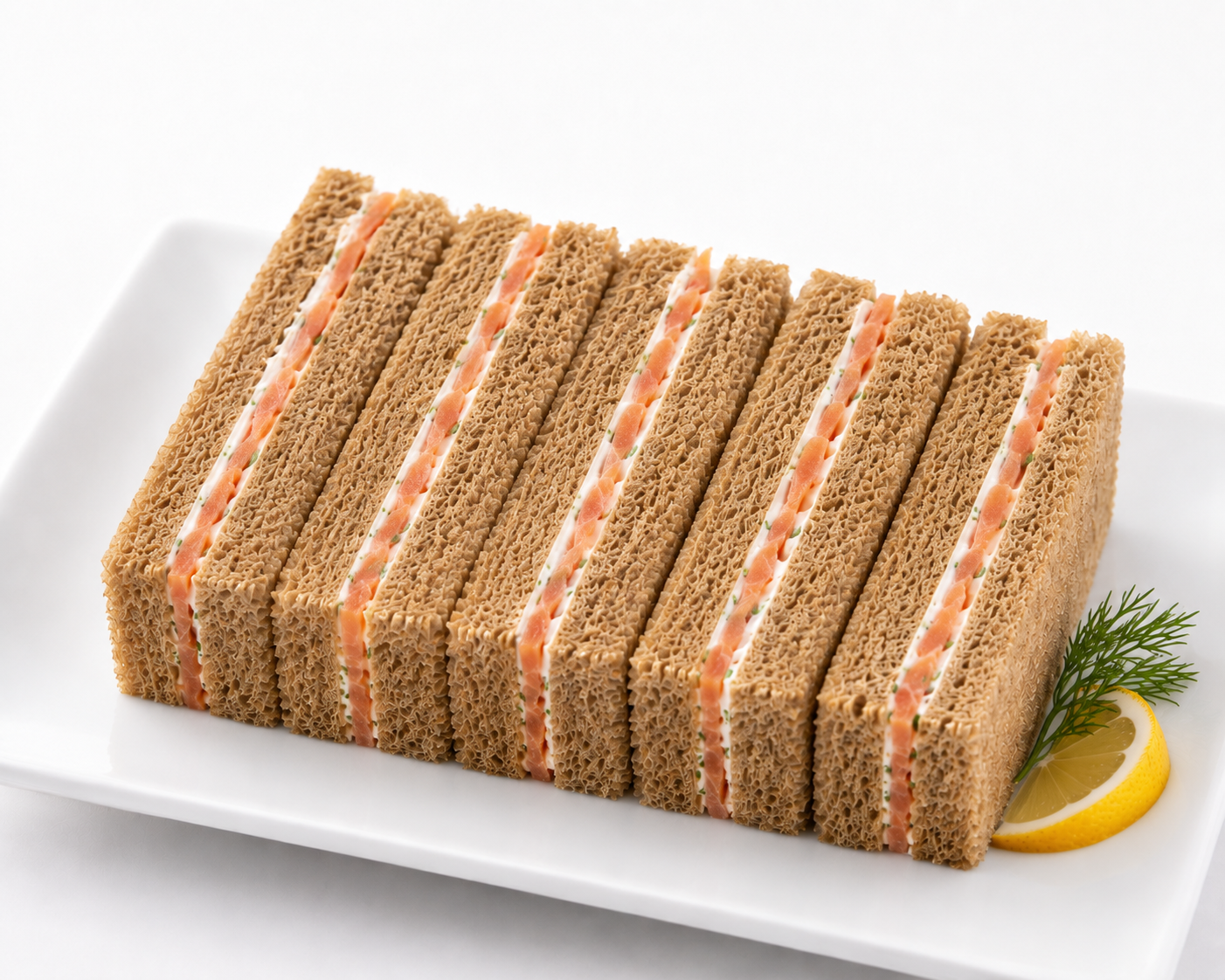 Row of sliced sandwiches on a white plate with a lemon wedge and dill garnish.