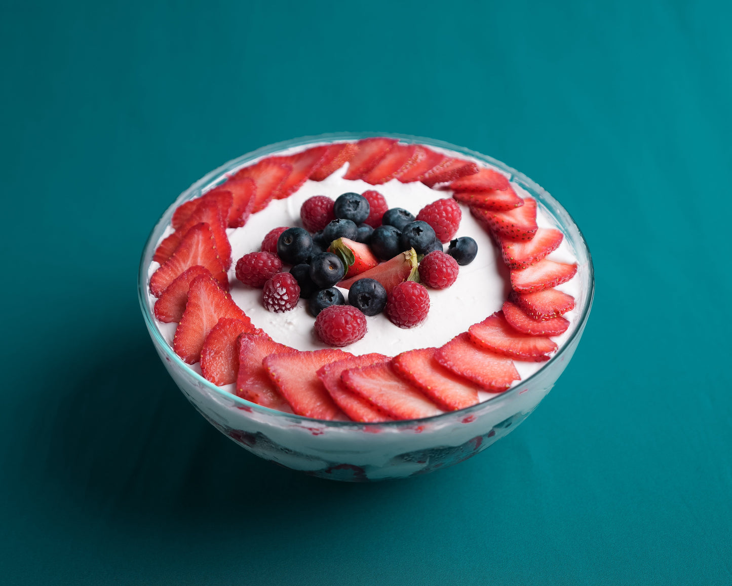 Bowl of dessert with strawberries and blueberries on a teal background
