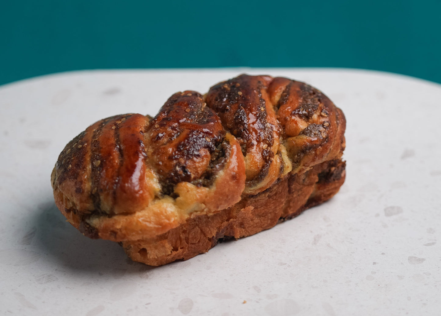 Braided bread loaf on a round stone surface with a teal background