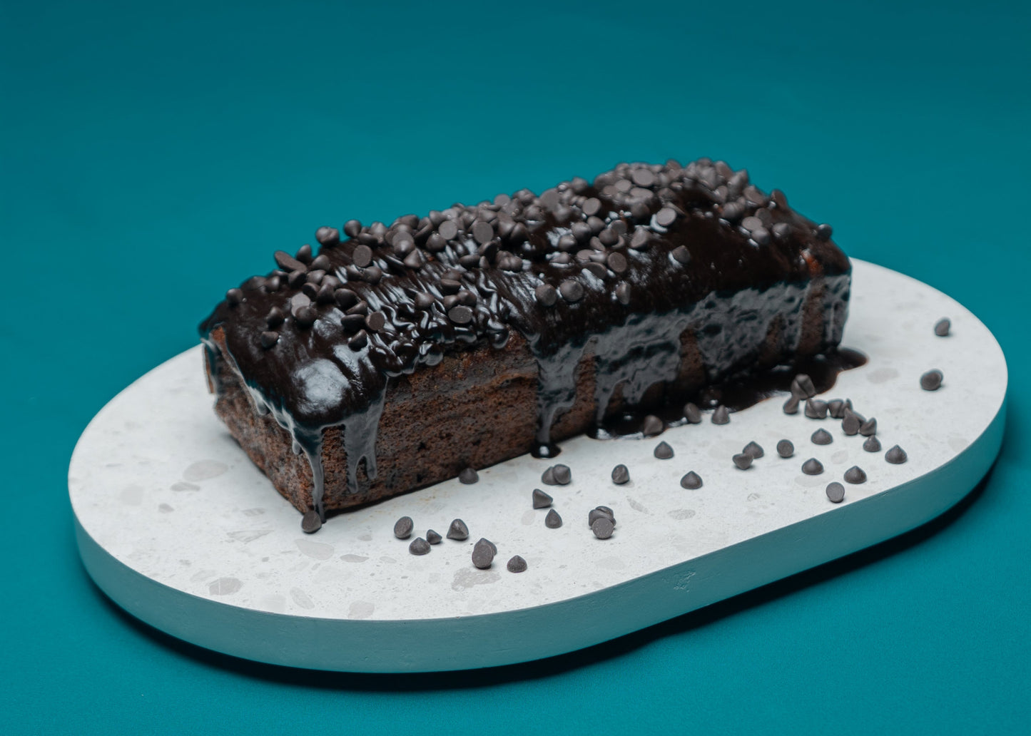 Chocolate loaf cake with chocolate chips on a white platform against a teal background