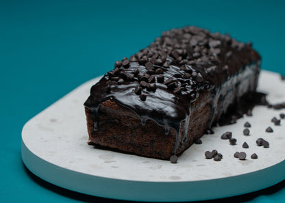 Chocolate loaf cake with chocolate frosting on a white plate against a blue background