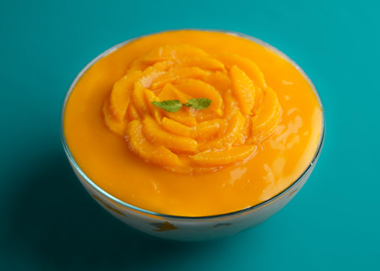 A top view of a Mango Trifle dessert with layers of cake and cream, garnished with a mango rose on top, on a teal background.